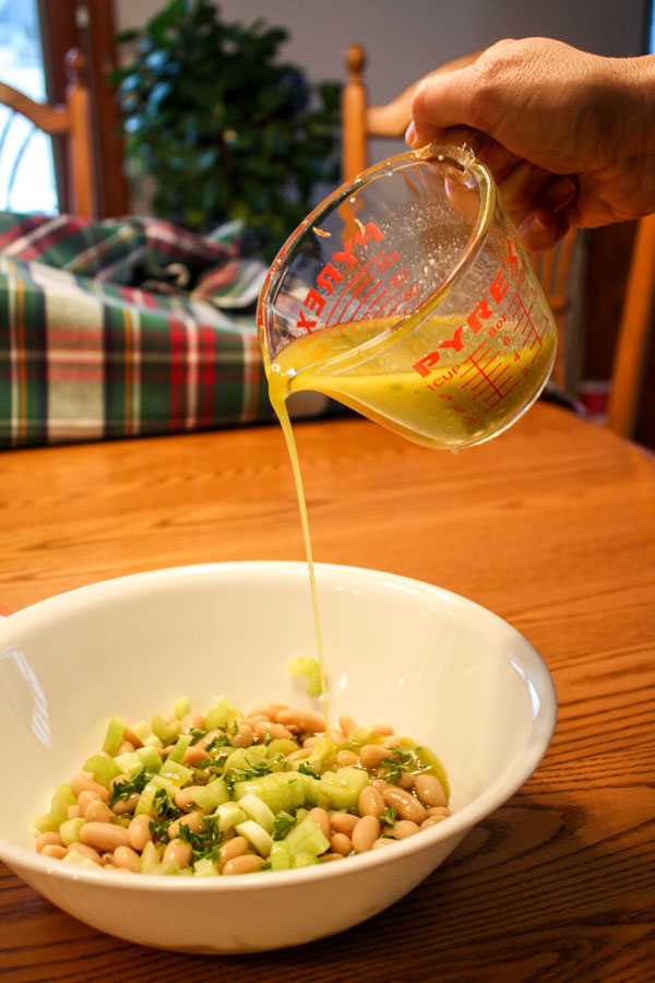 Vinagrette in Pyrex liquid measuring cup poured over white bean salad in white bowl