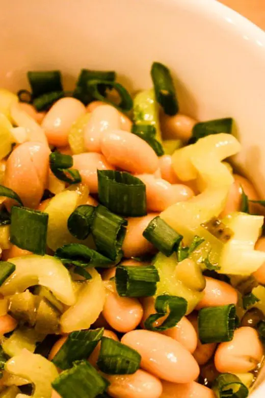 Spanish White Bean Salad in white bowl atop wooden table