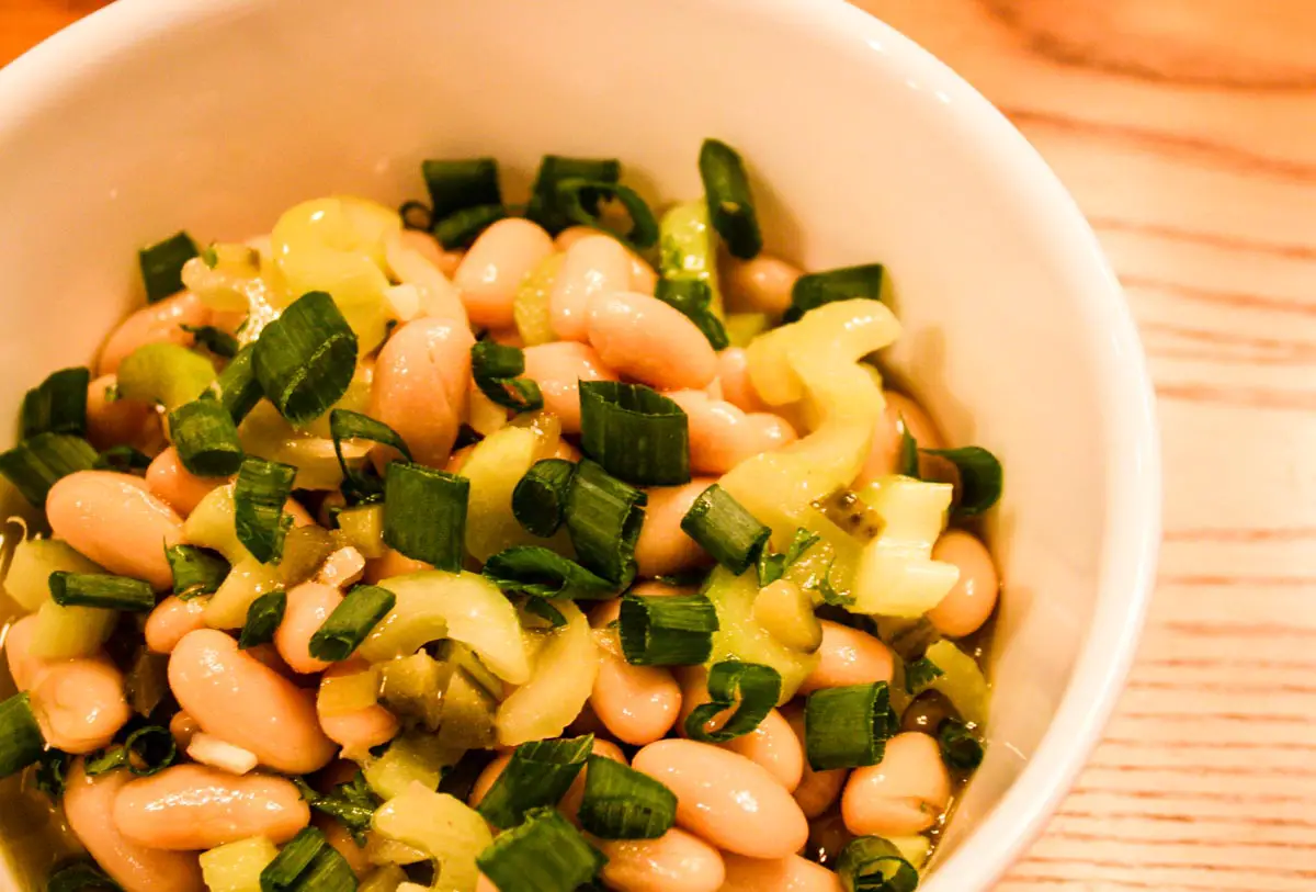 Spanish White Bean Salad in white bowl atop wooden table