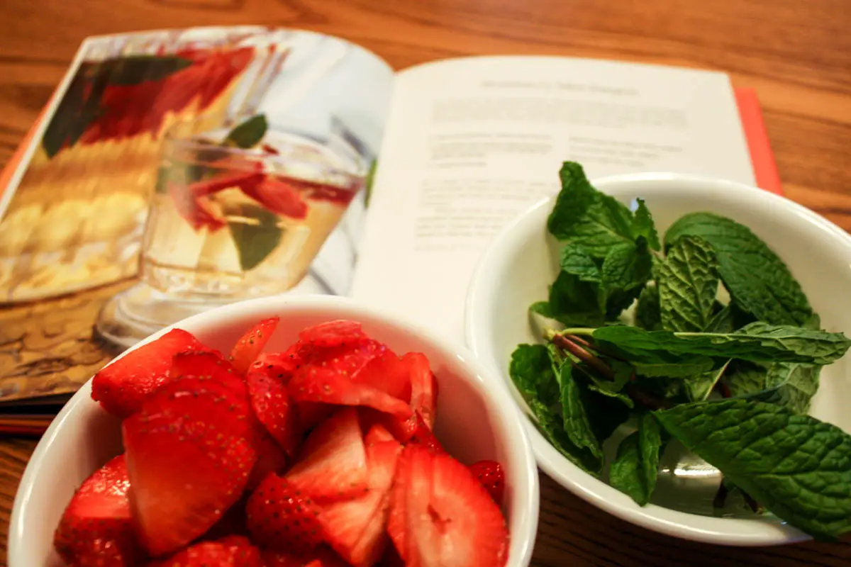 Strawberry Mint White Sangria recipe opened in cookbook with bowls sliced strawberries and mint leaves