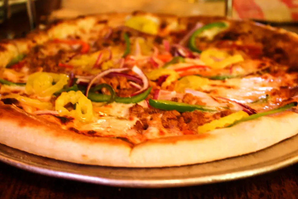 Thin-crust pizza topped with green bell and banana peppers and Italian sausage at Ottava Via