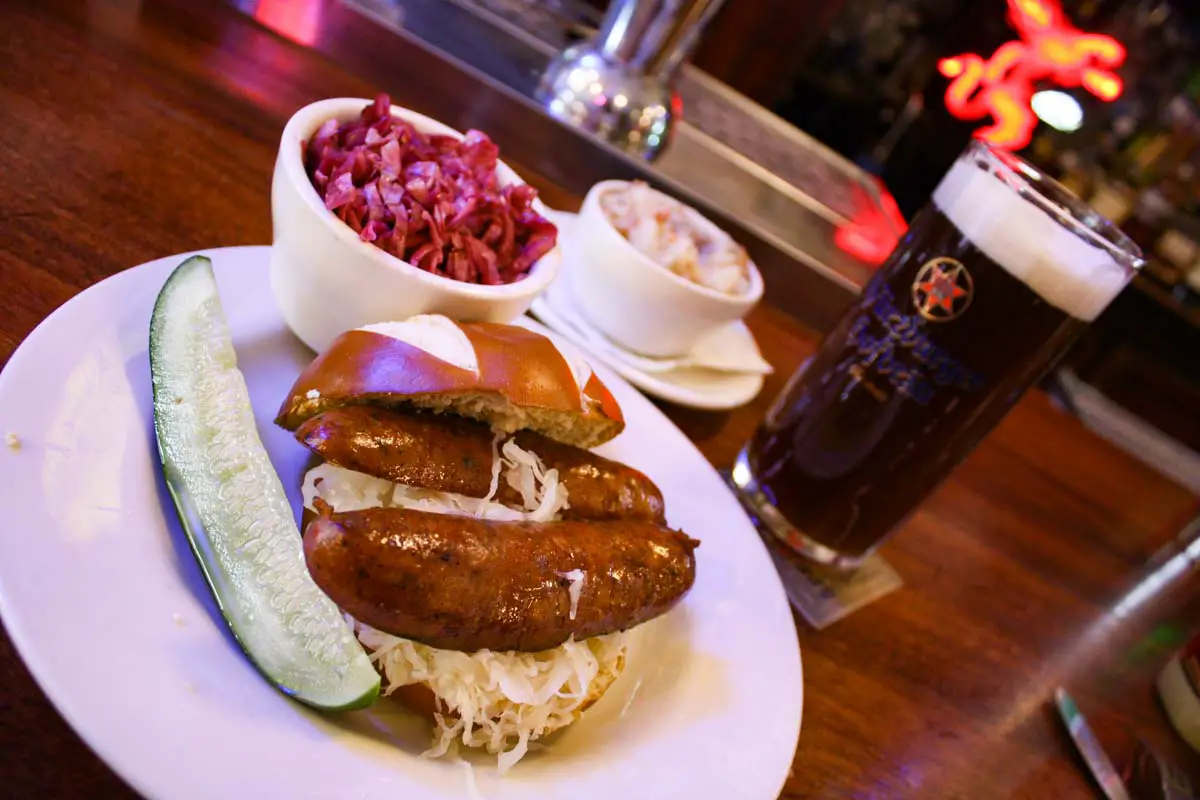 A wurst sandwich on a pretzel bun with sauerkraut with sides of red cabbage and potato salad with a Dunkel German beer at Jacob Wirth Restaurant in Boston
