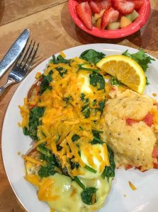 Breakfast of Florentine Eggs Benedict with tasty cheese grit casserole and a side of fresh fruit at Josie's in Lexington, Kentucky, USA