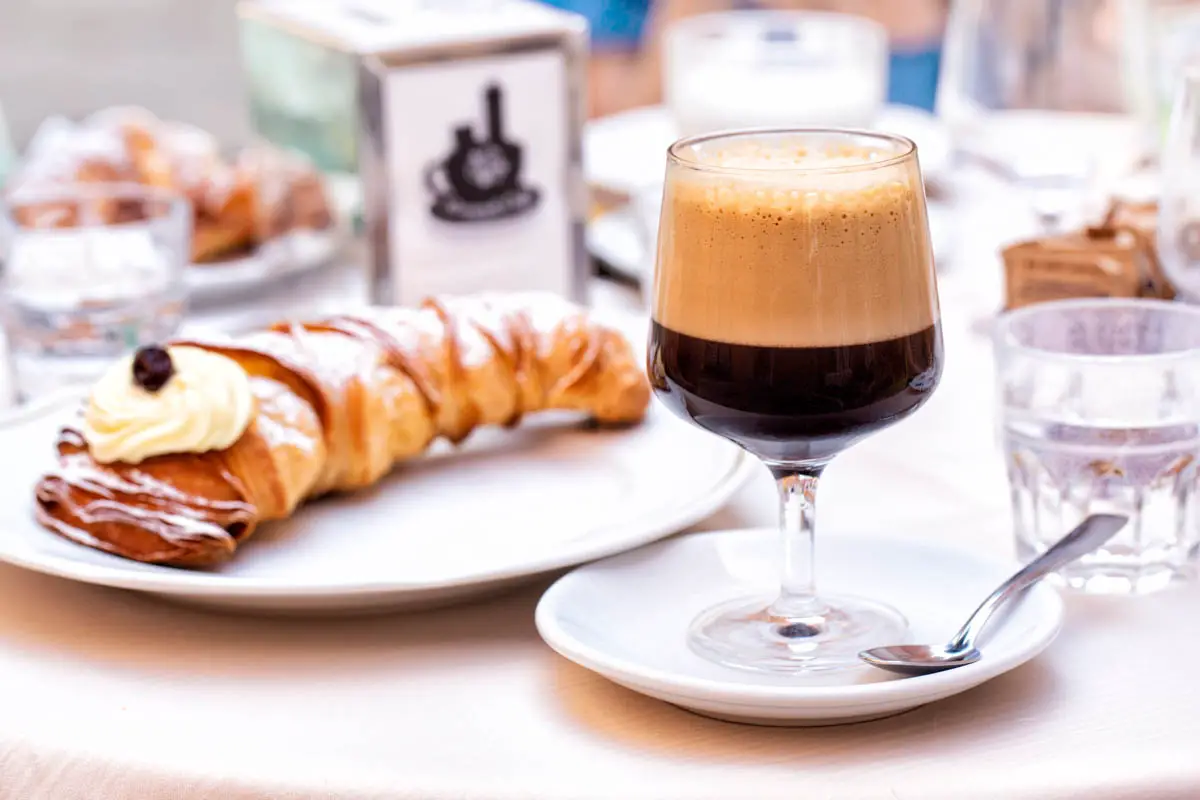 Italian breakfast table in a cafe. Caffè shakerato in a tall glass. Cold shaked coffee with a foam made with ice. A sfogliatella, or lobster tail, or coda d'aragosta, shell-shaped filled pastry with cream in Italy