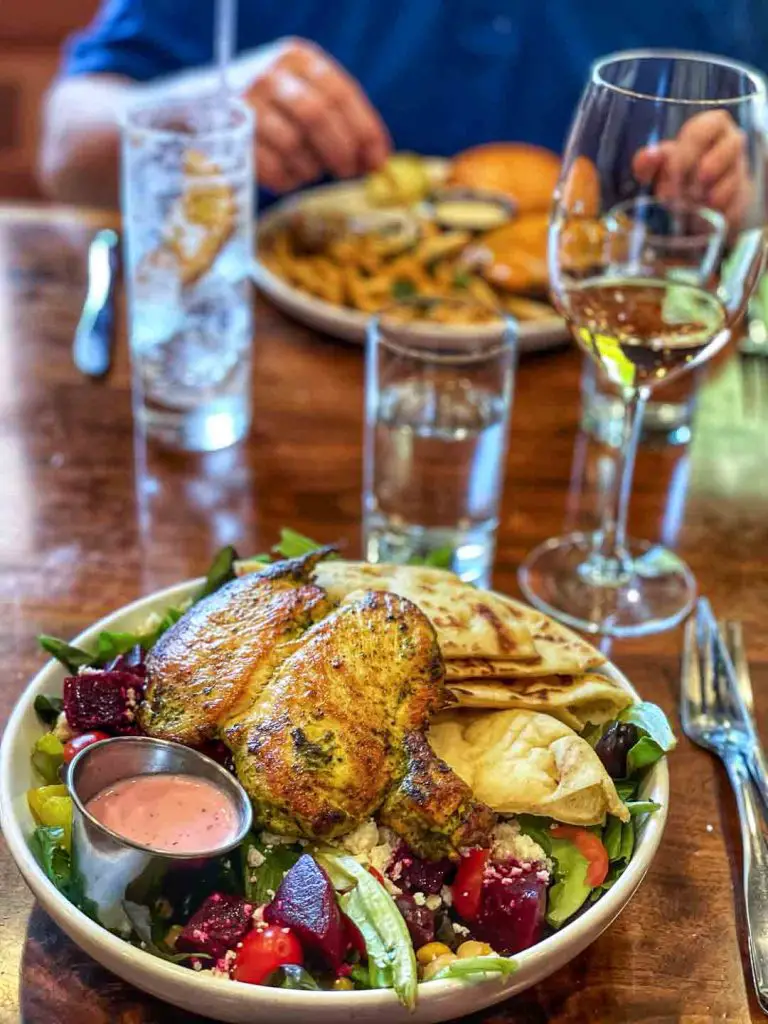 Sava's Greek salad with chicken and a Wagyu burger with fries in the background at Sava's restaurant in Ann Arbor, Michigan, USA