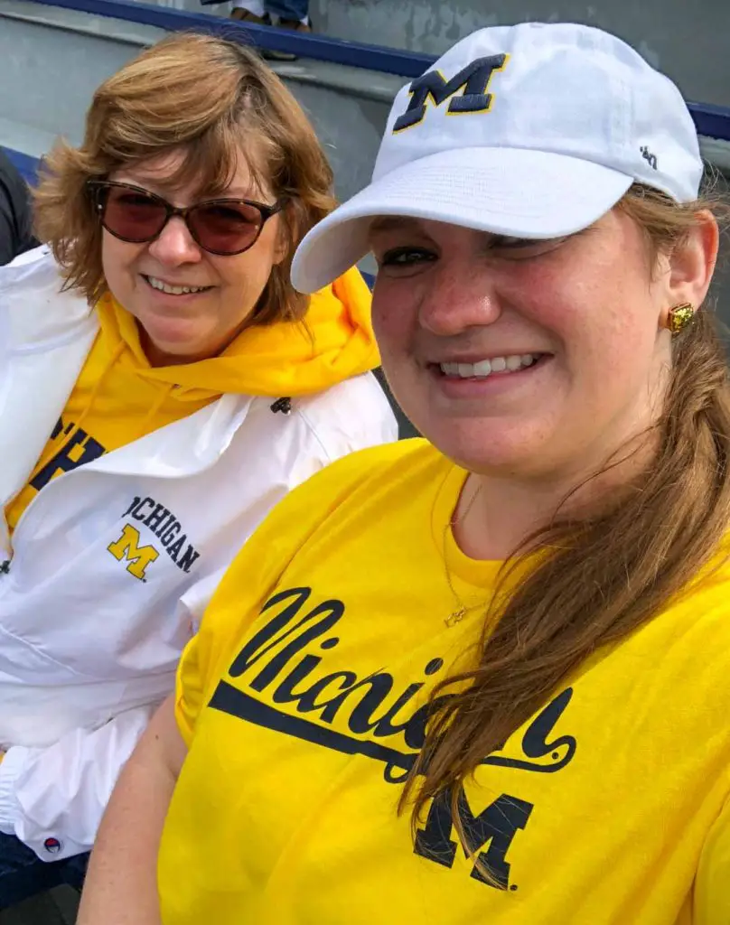 Michigan football fans clad in maize-and-blue apparel pose for a selfie in the stands of Michigan Stadium during a Michigan football game in Ann Arbor, Michigan