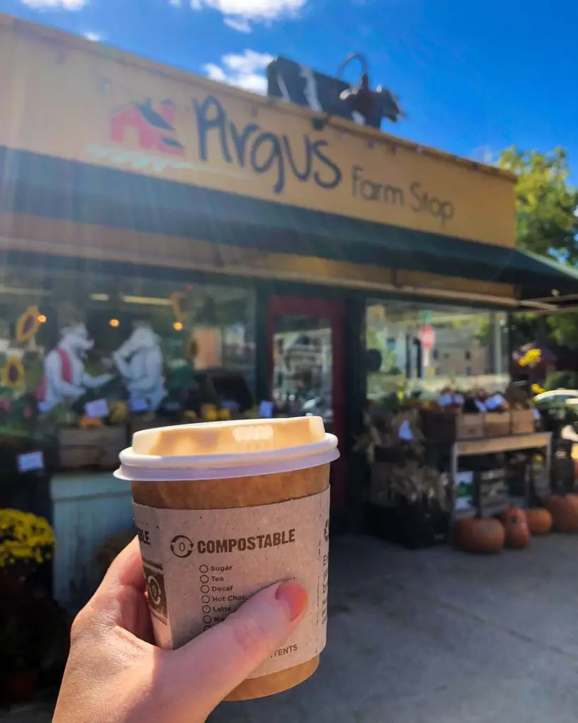 a woman holds a to-go coffee drink on a sunny fall day outside Argus Farm Stop in Ann Arbor, Michigan, USA