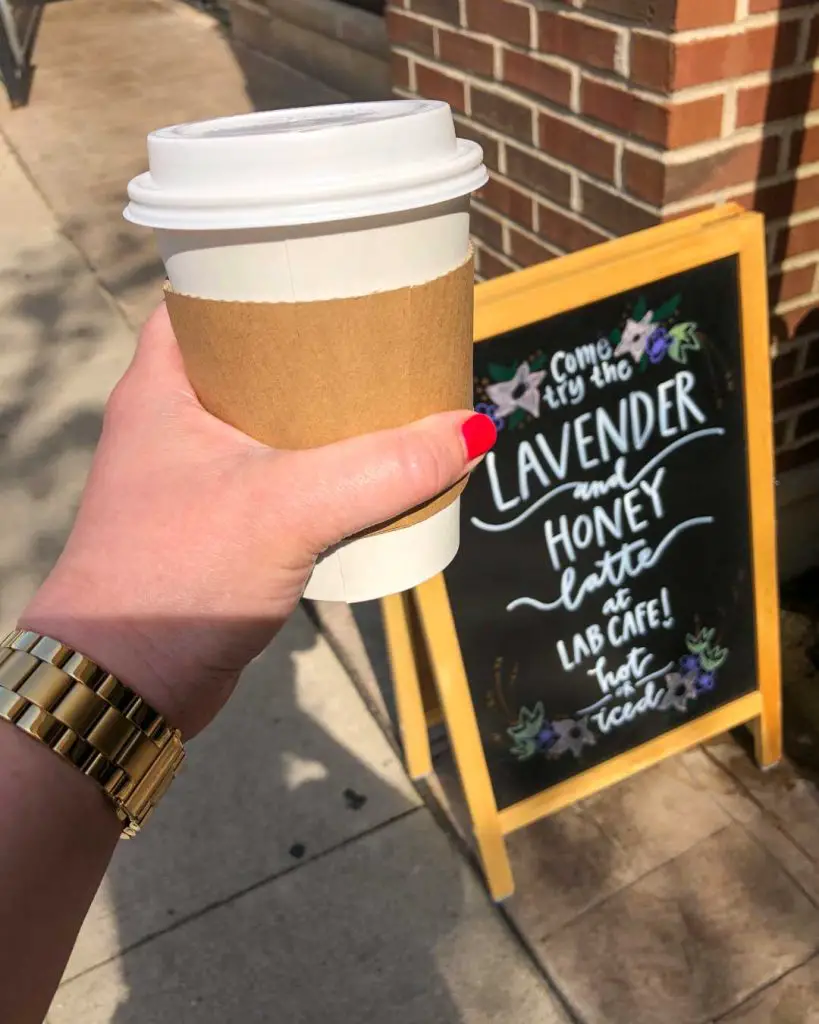 Lavender honey latte in a to-go coffee cup held in a woman's hand outside LAB CAFE in Ann Arbor, Michigan, USA