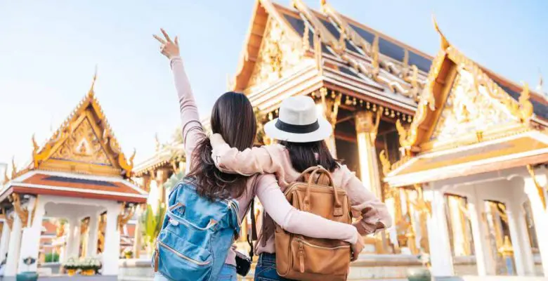 Two female friends face temple in Thailand with arms around each other