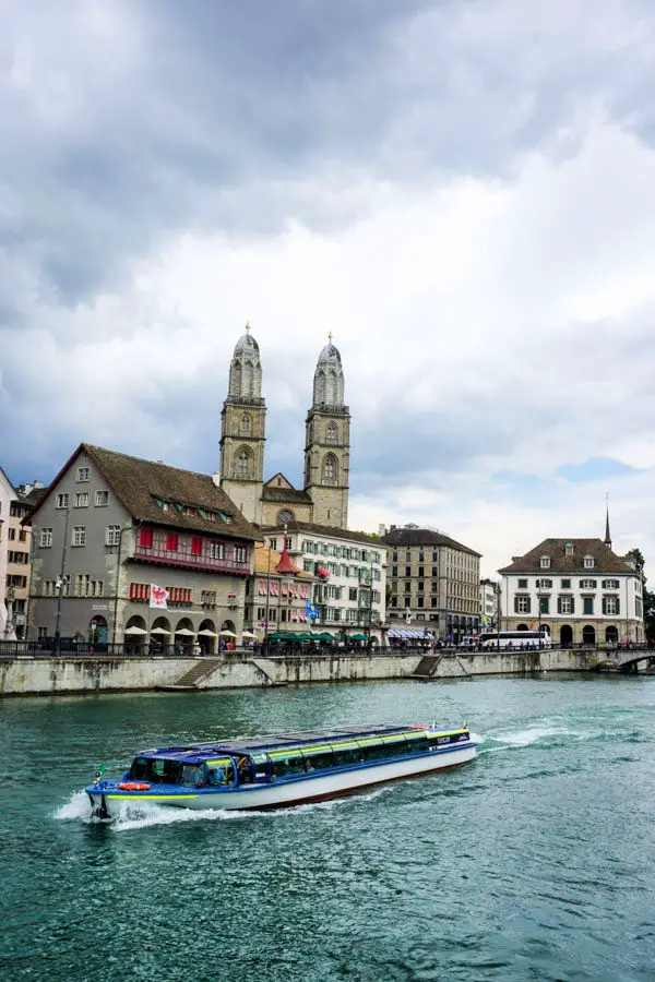 Riverboat cruises along Limmat River in Old Town Zurich with Grossmuenster cathedral in background