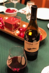 Stone Hill Winery 2015 Chambourcin in bottle and stemless wine glass on green cloth-covered table decorated for Christmas