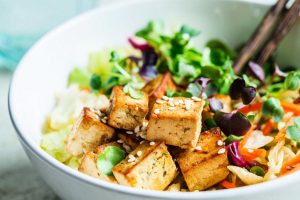 Fried tofu salad with sprouts and sesame seeds in a white bowl