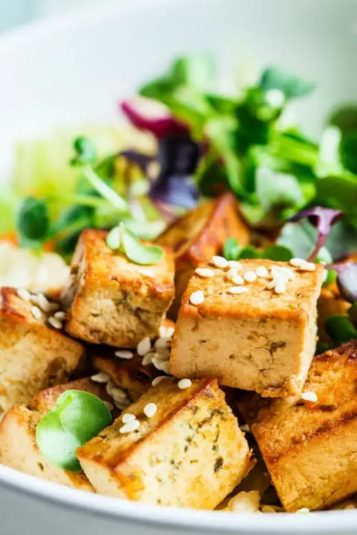 Fried tofu salad with sprouts and sesame seeds in a white bowl