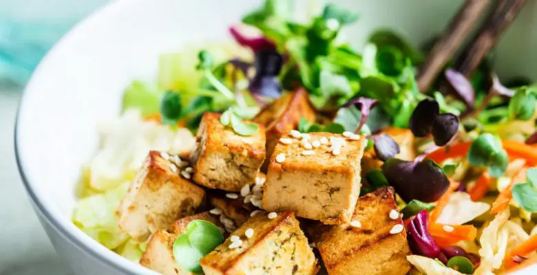 Fried tofu salad with sprouts and sesame seeds in a white bowl