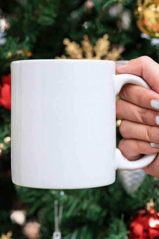 Woman holds white ceramic coffee mug in front of Christmas tree