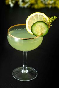 Green mimosa in gold-rimmed coupe glass with lemon and cucumber garnish