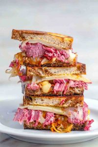 Corned beef melt sandwiches stacked on white plate