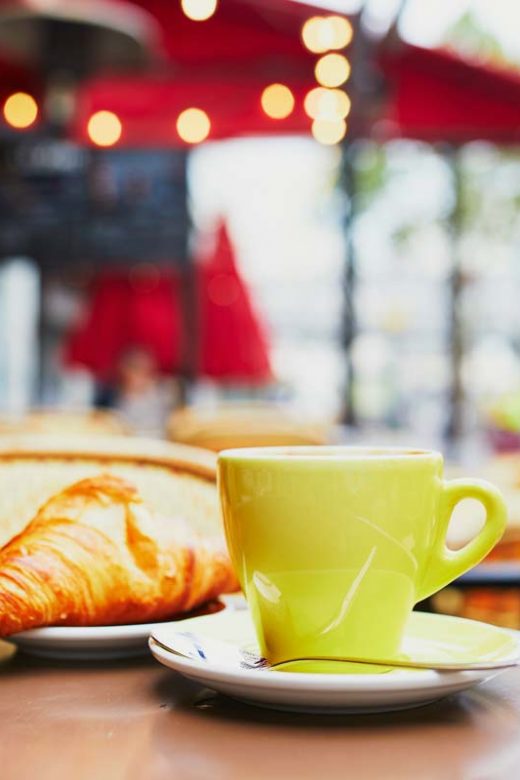 Cup of espresso coffee and croissant pastry on outdoor table of cafe in Paris, France