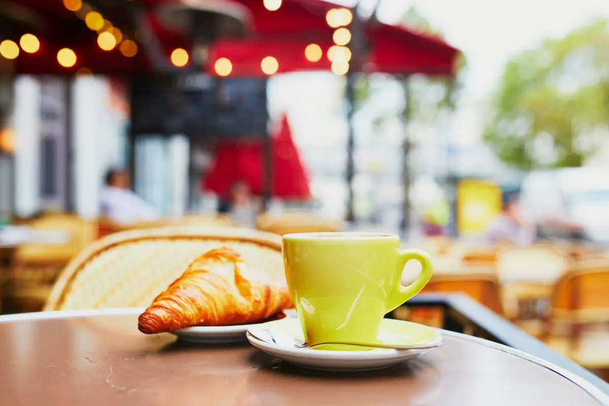 Cup of espresso coffee and croissant pastry on outdoor table of cafe in Paris, France