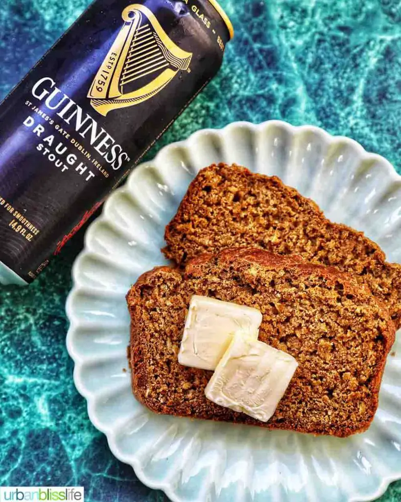 Flat lay of scalloped dish plated with two slices of Guinness brown bread topped pats of butter next to Guinness beer can flat lay