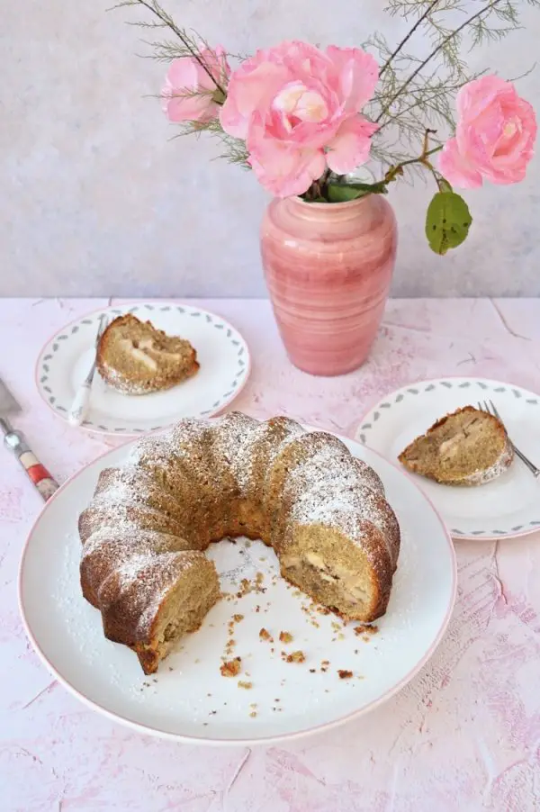 Irish apple cake bundt cake sliced and displayed on table with pink vase filled with pink flowers