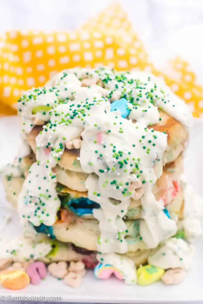 Stack of Lucky Charms pancakes topped with white chocolate "syrup" and green sprinkles 