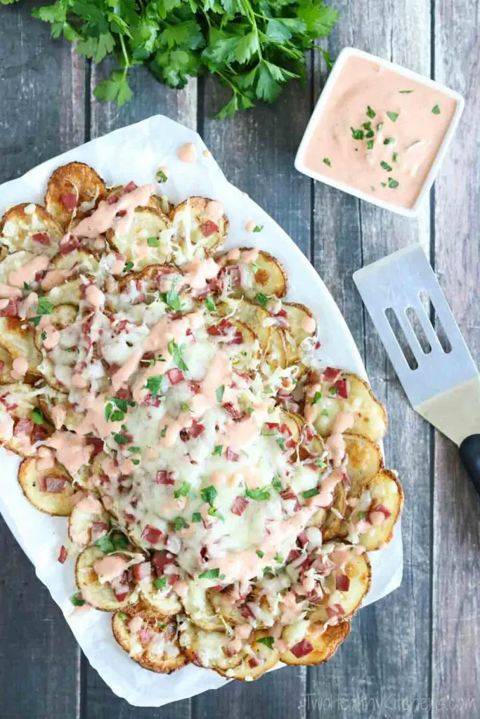 Plate of Reuben-topped nachos with dipping sauce and serving utensil on the side