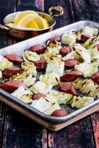 Sheet pan with roasted cabbage and sausage with side dish of lemon wedges