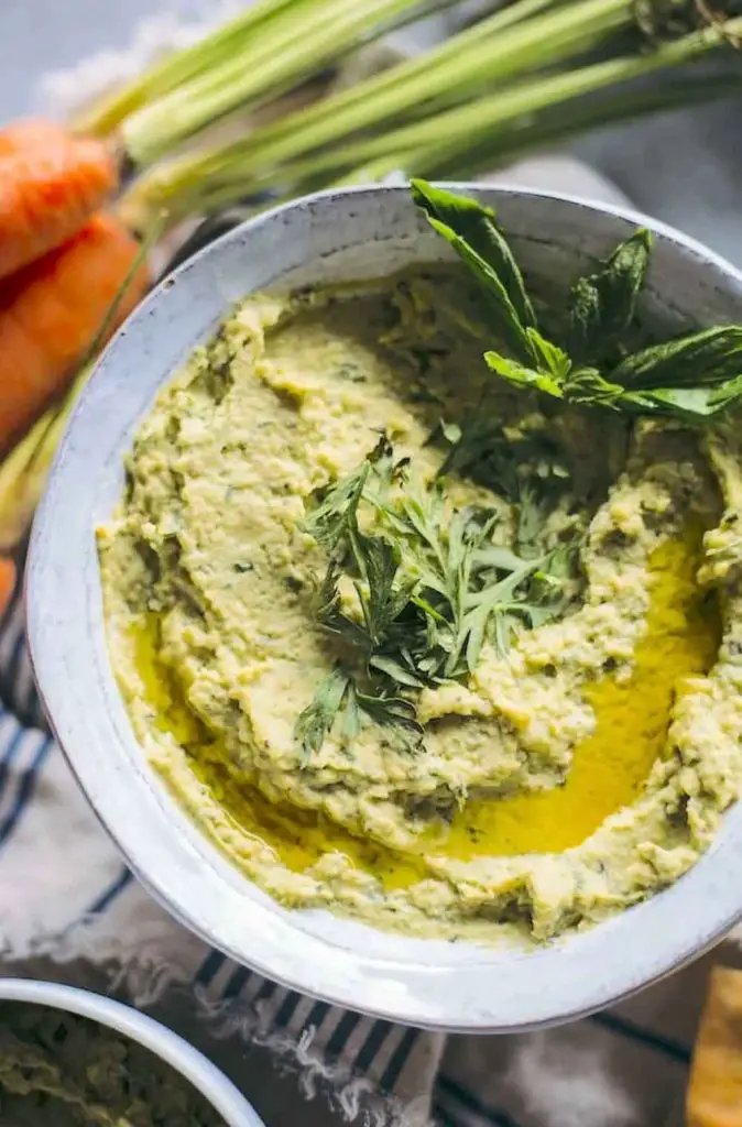 Carrot-top pesto hummus in a bowl with carrots in background