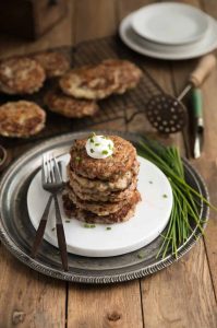 Stack of Irish corned beef potato pancakes on plate with more on cooking rack in background