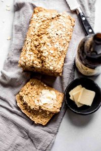 Guinness bread loaf with two slices next to Guinness beer bottle and small dish containing pats of butter