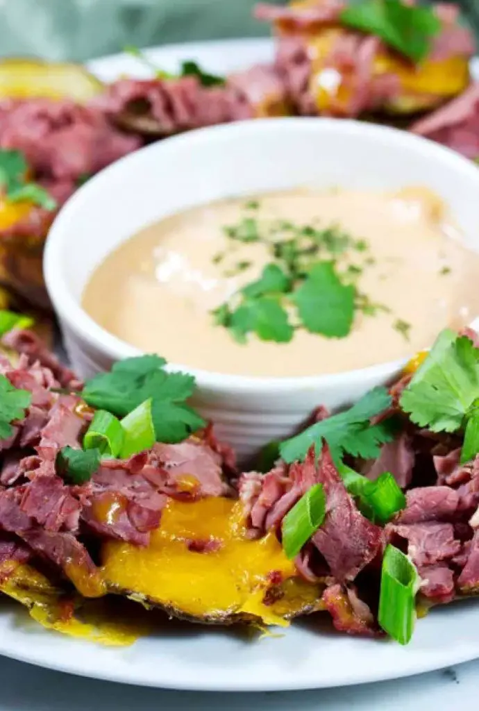 Gluten-free Irish nachos topped with corned beef plated around dipping sauce
