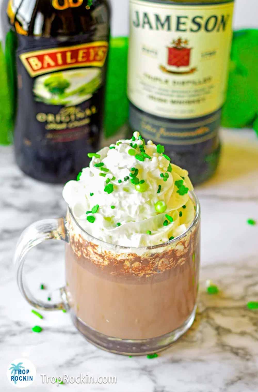Irish hot chocolate in clear mug with Baileys Irish Cream and Jameson Irish Whiskey bottles in background