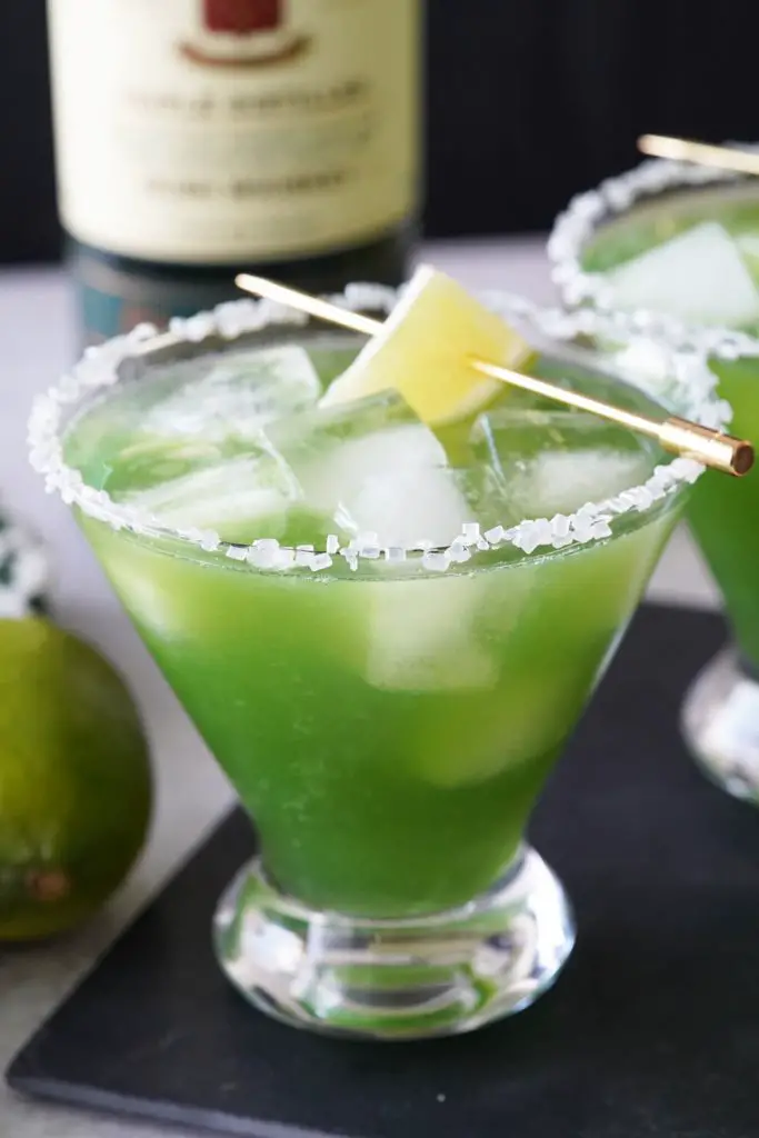 Green "shamrock" margaritas in stemless martini glasses with Irish whiskey bottle in background