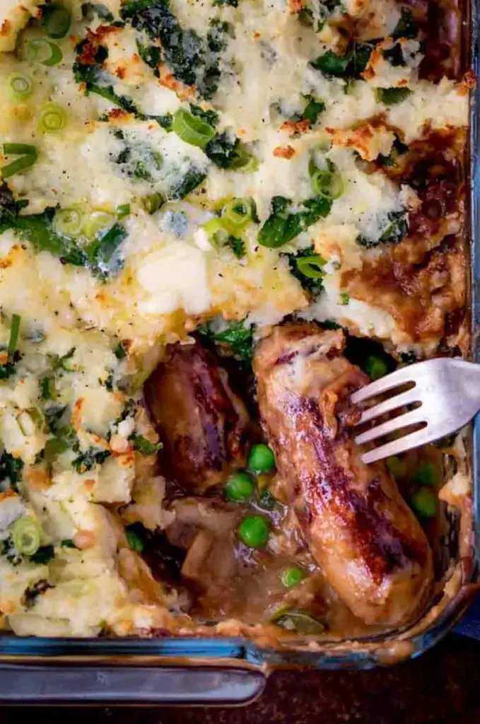 Fork pulling sausage from casserole dish of sausage-and-colcannon bake