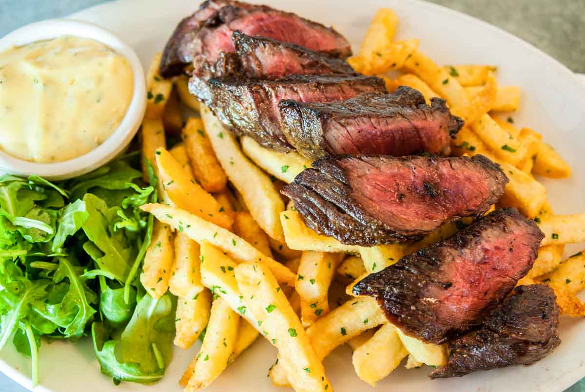 Steak Frites with greens and dipping sauce on white plate