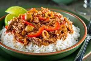 Cuban ropa vieja with lime wedges on a bed of rice in a green bowl
