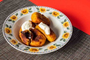 Guatemalan Rellentios de Platanos, a Guatemalan dish of stuffed plantains, sit on a round white dish decorated with sunflowers around the rim