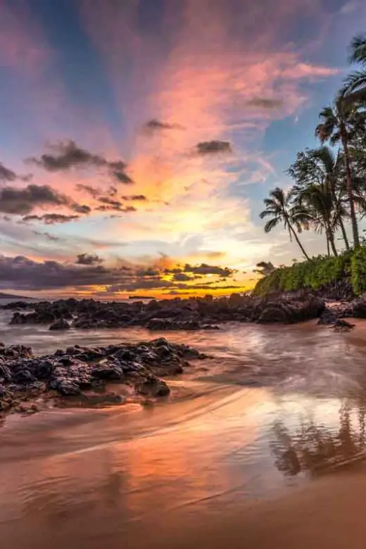 A colorful sunset paints the sky shades of purple, pink, and orange at a secret cove on Maui, Hawaii