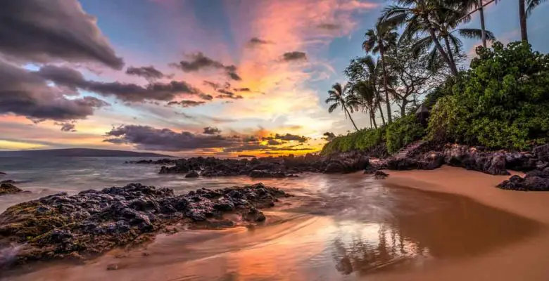 A colorful sunset paints the sky shades of purple, pink, and orange at a secret cove on Maui, Hawaii