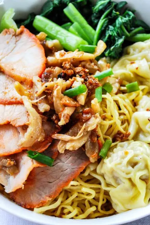 Wanton mee dish of egg noodles, sliced pork, and wantons in a white bowl with chopsticks