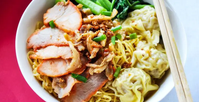 Wanton mee dish of egg noodles, sliced pork, and wantons in a white bowl with chopsticks