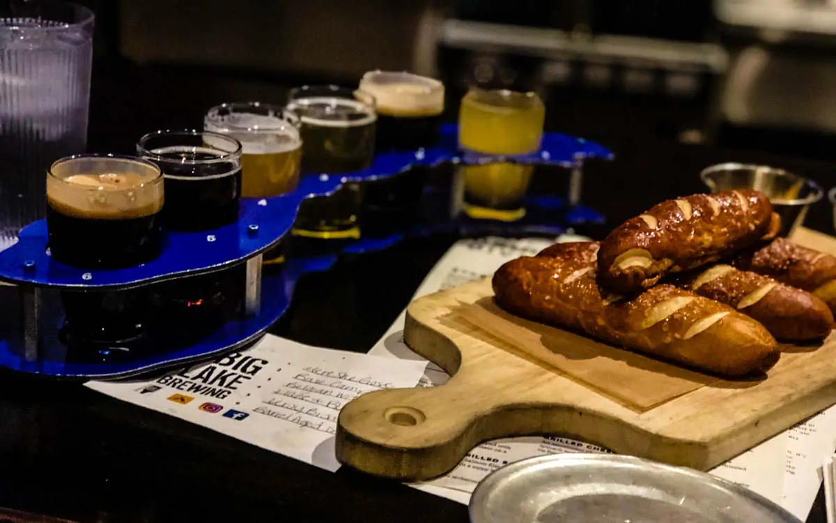 Craft beer flight in drink holder shaped like Lake Michigan next to soft pretzel sticks on wooden board at Big Lake Brewing 