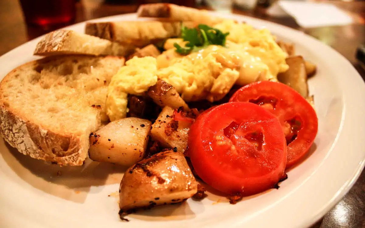 Hippy Hash breakfast dish with sourdough toast, two roma tomato slices, and scrambled eggs atop Dutch potatoes