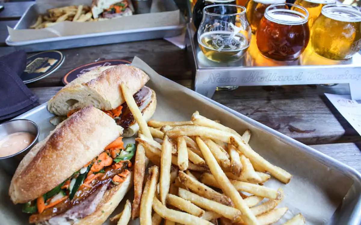 Bahn Mi sandwich with fries and beer flight in background at New Holland Brewpub in Holland, Michigan
