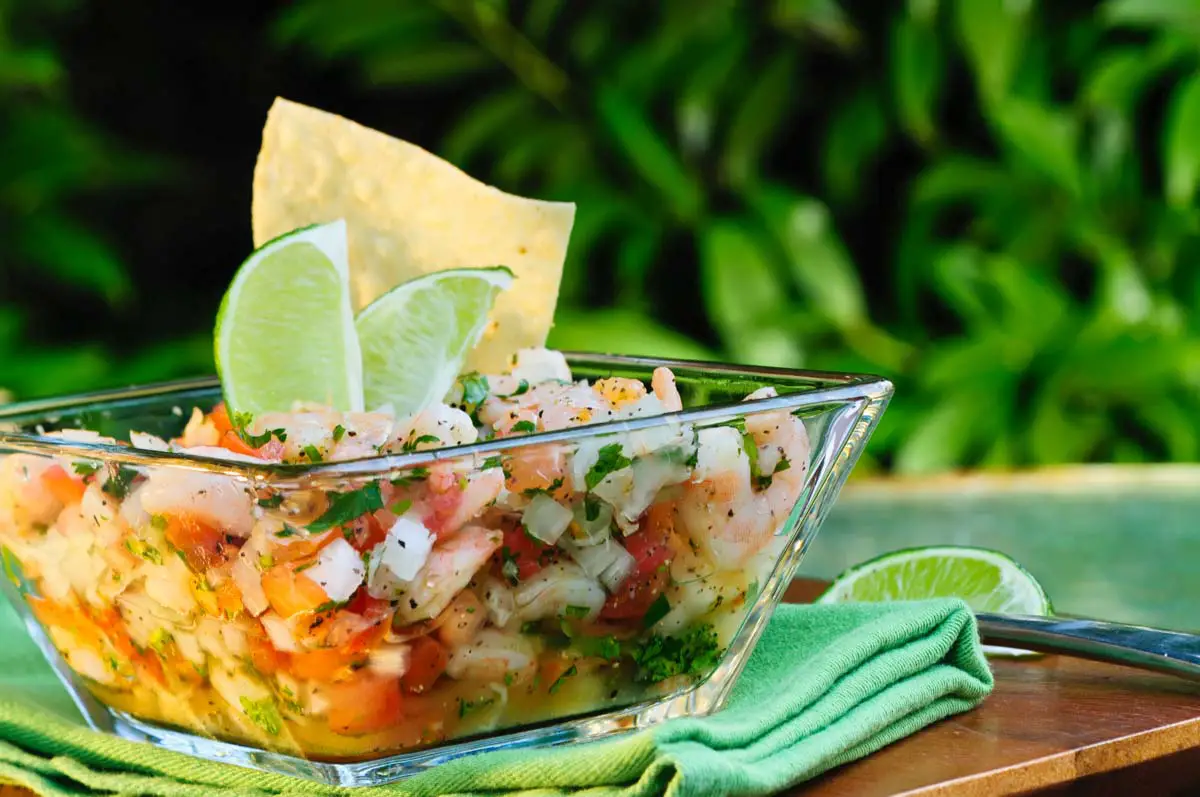 Mexican-style ceviche garnished with lime wedges and tortilla chip in glass bowl