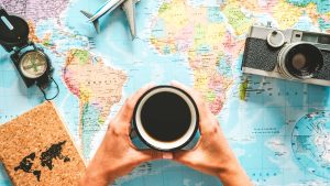 Gift ideas for coffee travelers banner image with a traveler holding a cup of coffee over a world map with travel gear around the map
