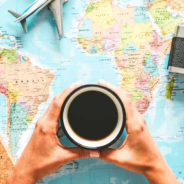 Gift ideas for coffee travelers banner image with a traveler holding a cup of coffee over a world map with travel gear around the map