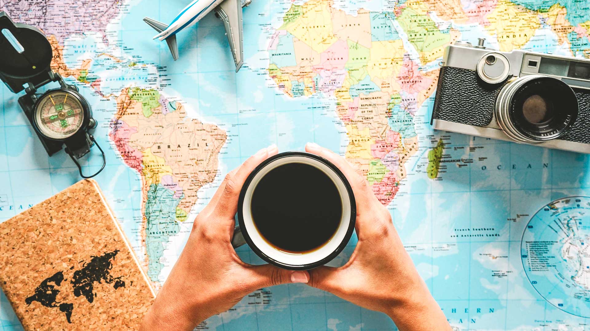Gift ideas for coffee travelers banner image with a traveler holding a cup of coffee over a world map with travel gear around the map