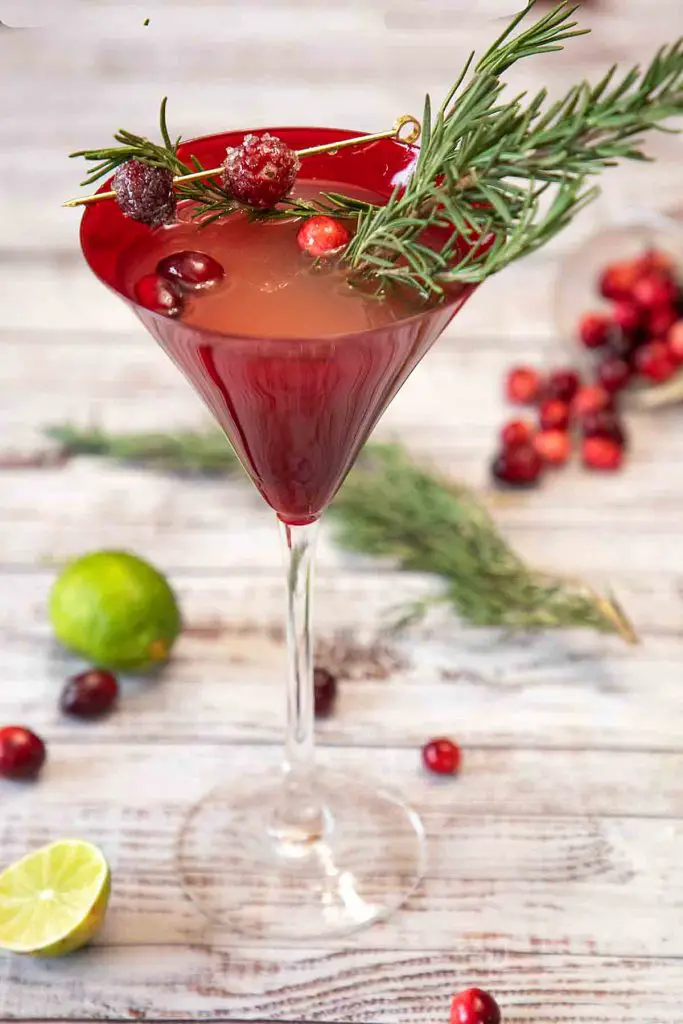 Cosmopolitan cocktail in a red martini glass with rosemary springs and fresh cranberry garnishes